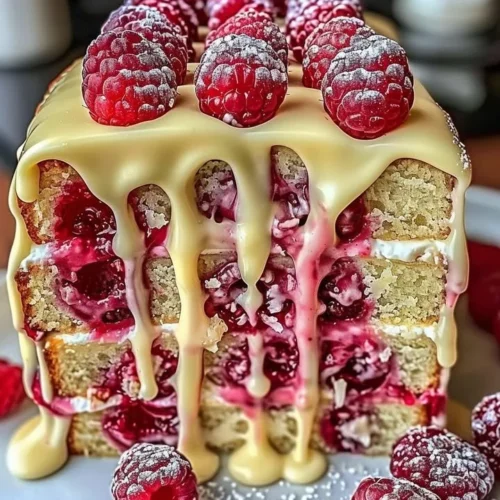 Heavenly white chocolate raspberry cake adorned with fresh raspberries and white chocolate shavings.