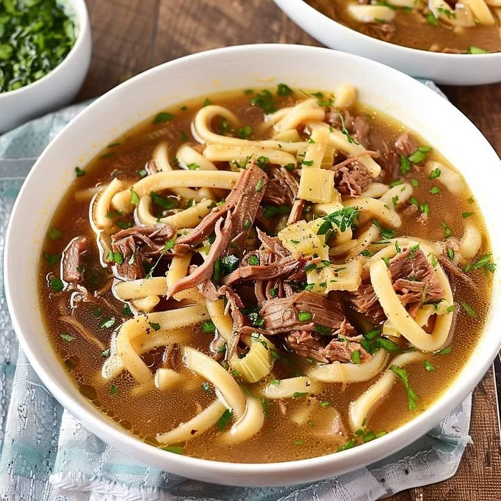 Delicious slow-cooked beef noodle soup in a bowl garnished with fresh herbs.