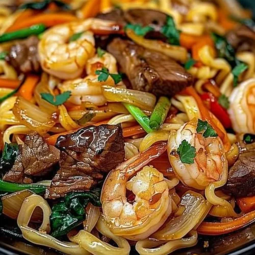 Plate of Steak and Shrimp Stir-Fried Noodles garnished with veggies.